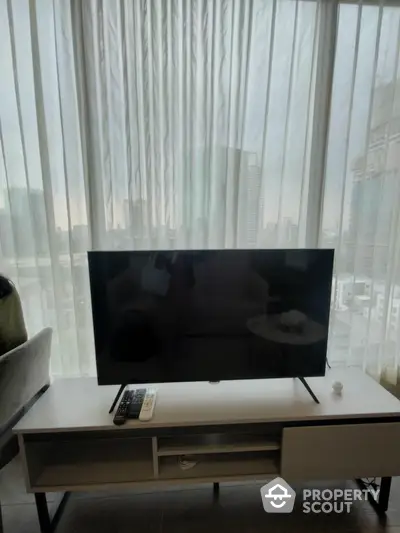 Modern living room with a large flat-screen TV and sheer curtains, offering a blend of comfort and contemporary urban living.