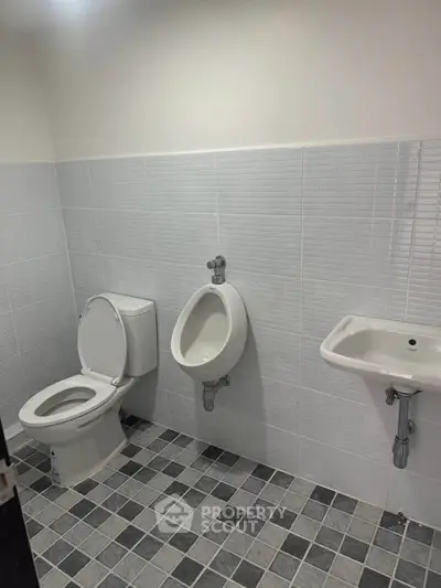 Modern bathroom with tiled walls and floor, featuring toilet, urinal, and sink.