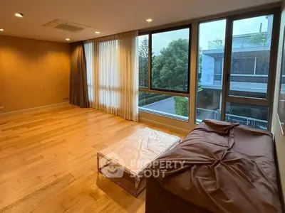 Spacious living room with large windows and wooden flooring, offering a serene view of greenery.