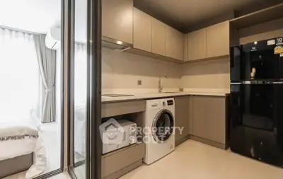 Modern kitchen with washing machine and microwave, adjacent to a cozy bedroom.