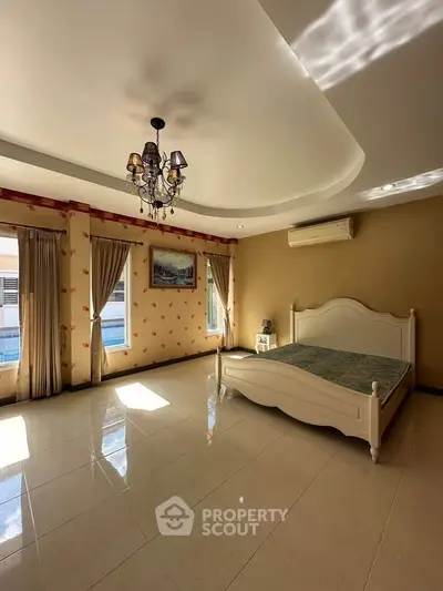 Spacious bedroom with elegant chandelier and large windows offering natural light.