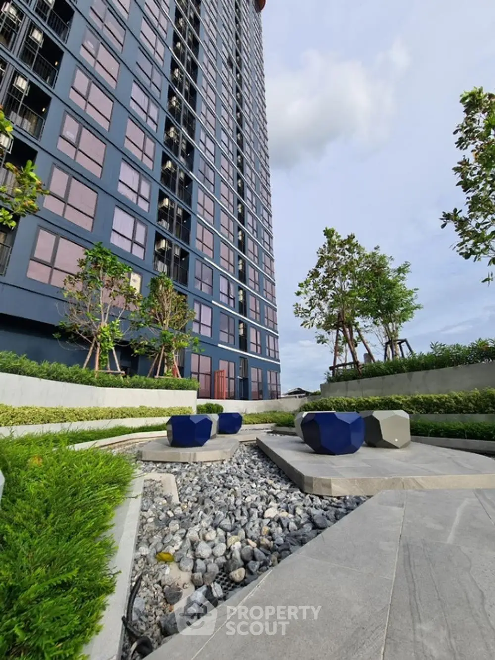 Modern high-rise building with landscaped garden and seating area, perfect for urban living.