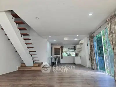Spacious open-plan living room with modern staircase and large windows offering garden views.