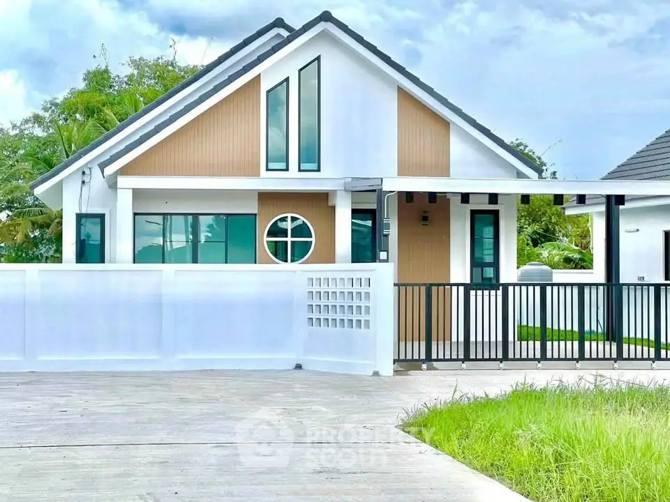 Modern single-story house with unique circular window and stylish facade, surrounded by lush greenery.