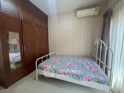 Cozy bedroom with floral bedding and built-in wardrobe, featuring natural light and air conditioning.