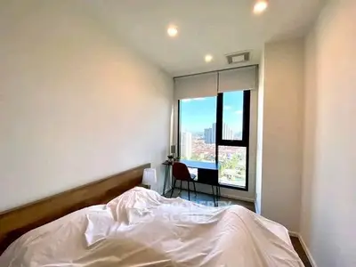 Bright bedroom with city view and modern decor, featuring a cozy bed and desk by the window.