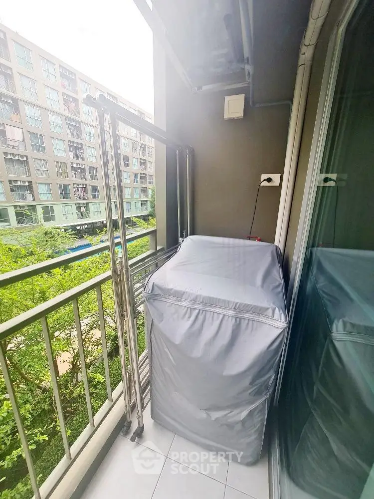 Compact balcony with covered washing machine and view of modern apartment complex.