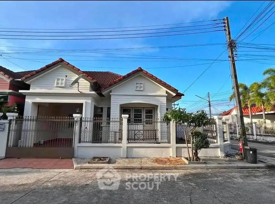 Charming single-story house with red roof and gated entrance in a serene neighborhood.