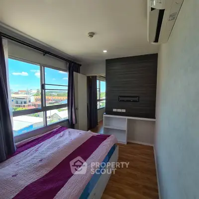 Bright bedroom with large window offering stunning city views, featuring modern decor and wooden flooring.