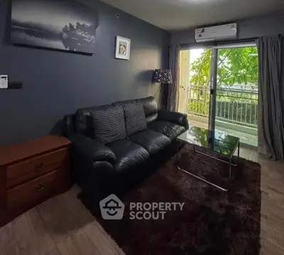 Cozy living room with black leather sofa, glass coffee table, and balcony view.