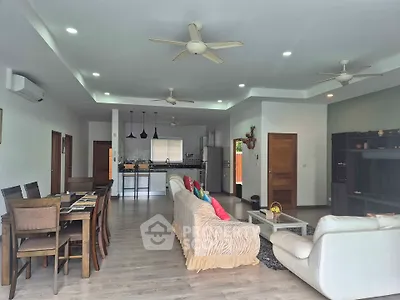 Spacious open-plan living room with modern kitchen and dining area, featuring ceiling fans and stylish decor.