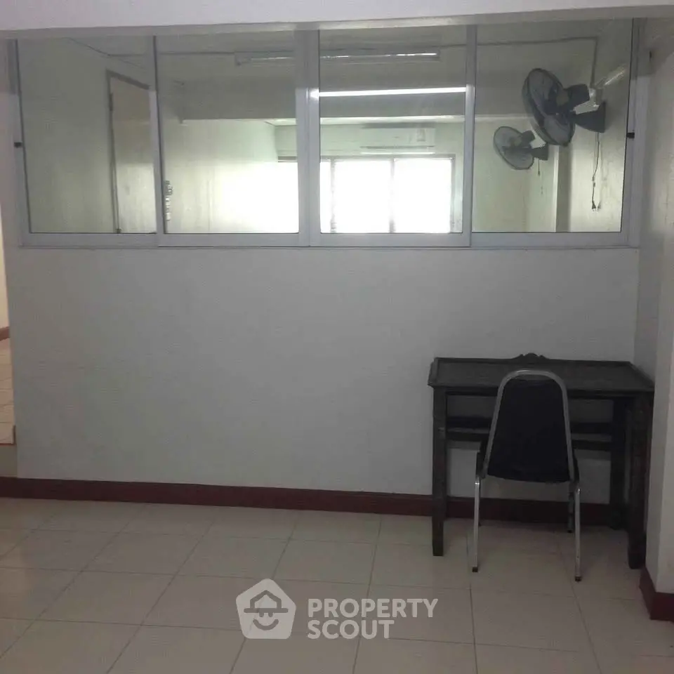 Spacious office space with glass partition and tiled flooring, ideal for a productive work environment.
