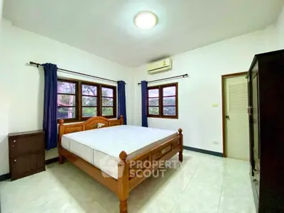 Spacious bedroom with wooden bed frame and large windows offering natural light.