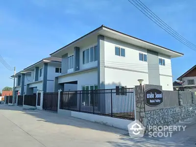 Modern two-story residential building with gated entrance and paved driveway in suburban area.