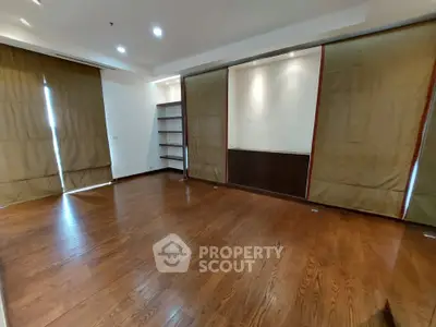 Spacious empty room with wooden flooring and large windows, ideal for customization.