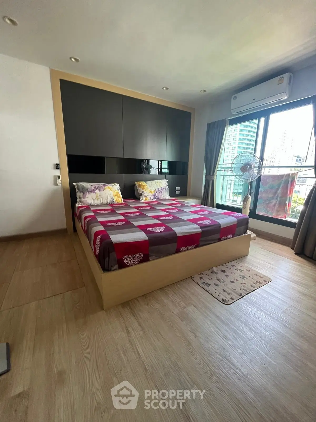 Modern bedroom with large window and city view, featuring stylish decor and wooden flooring.