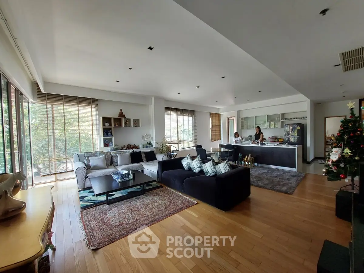 Spacious modern living room with open kitchen and large windows overlooking greenery.