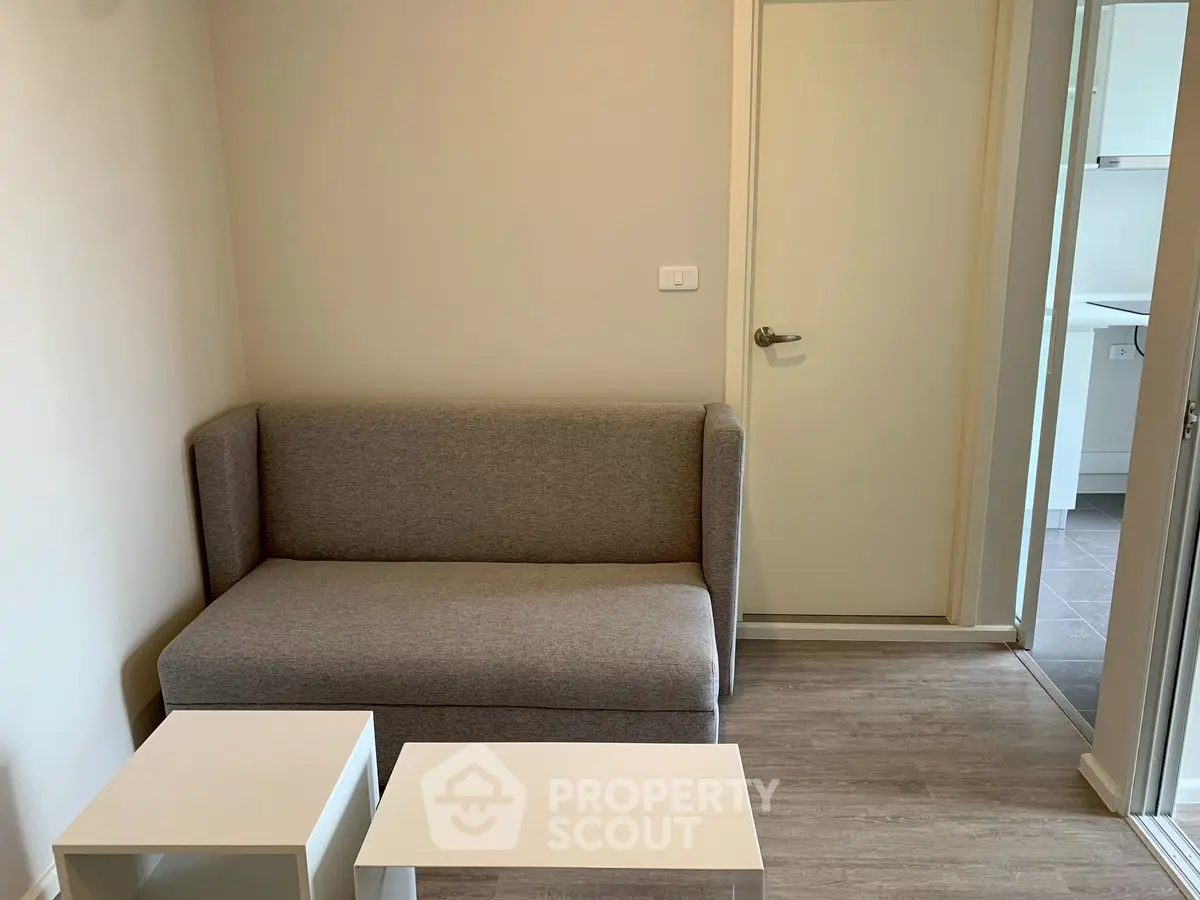 Cozy living room with modern gray sofa and white coffee tables in a compact apartment.