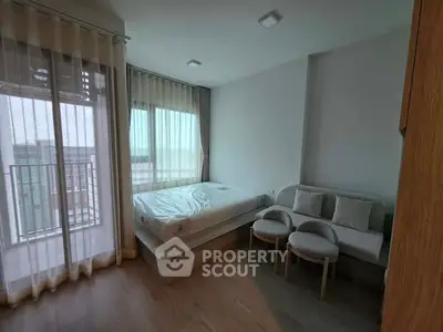 Modern bedroom with large windows and cozy seating area, featuring natural light and minimalist design.