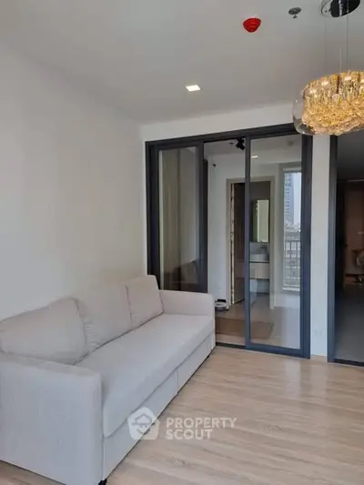 Modern living room with elegant chandelier and sliding glass doors leading to a bright balcony.