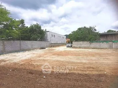 Spacious vacant land plot ideal for development with surrounding walls and trees.