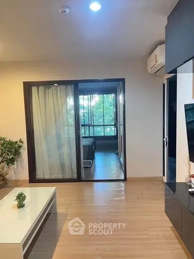Modern living room with sliding glass doors leading to a bedroom, featuring wooden flooring and air conditioning.