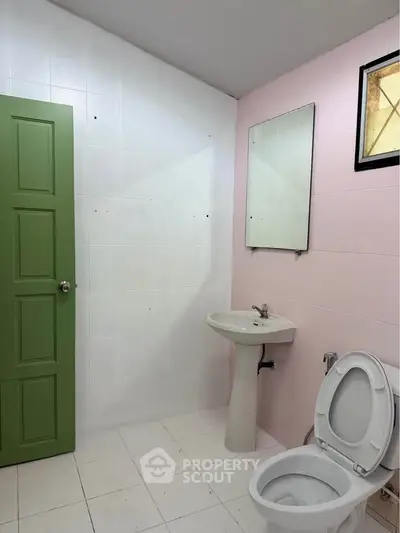 Spacious bathroom with green door and pink accent wall, featuring a pedestal sink and toilet.