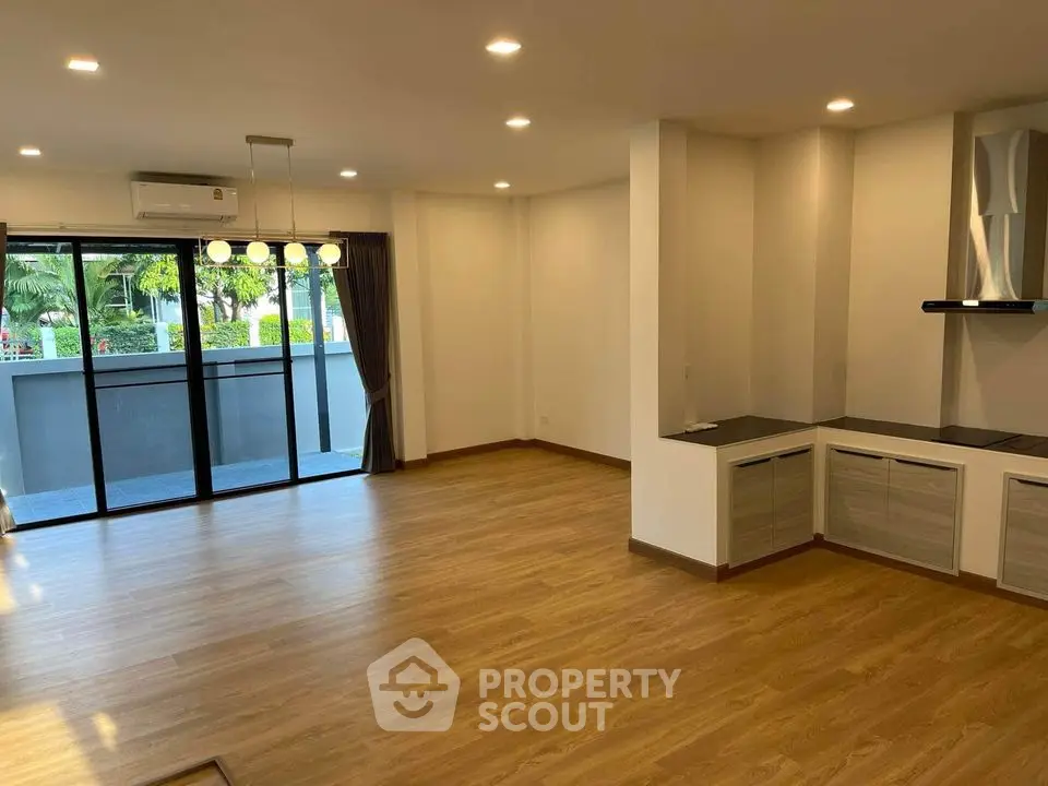 Spacious open-plan living area with modern kitchen, ample natural light, and a view of greenery through large balcony doors, perfect for entertaining and relaxation.