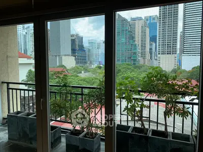 Stunning cityscape view from a balcony with lush greenery and modern skyscrapers.