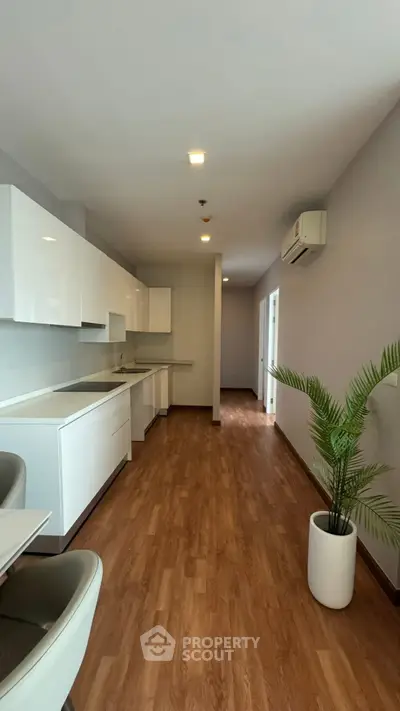 Modern kitchen with sleek white cabinets and wooden flooring, featuring an open layout and stylish decor.