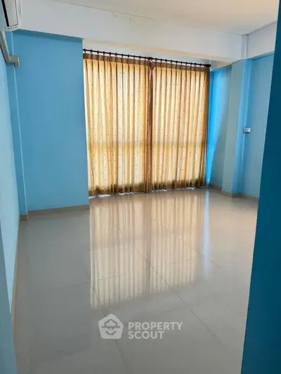 Spacious empty room with blue walls and large window, perfect for customization.