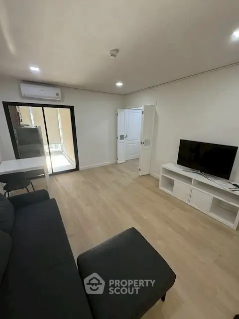 Modern living room with sleek furniture and natural light, featuring a TV and air conditioning.