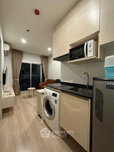 Modern apartment interior with open kitchen and living area, featuring washing machine and microwave.