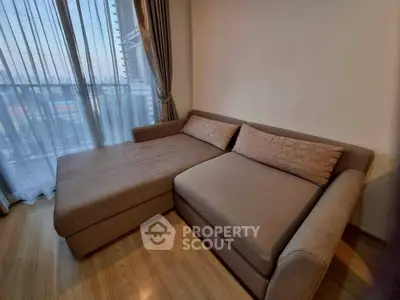 Cozy living room with stylish sofa and floor-to-ceiling windows offering natural light and city views.