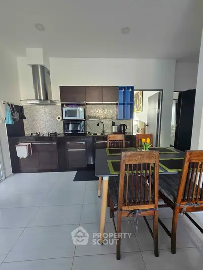 Modern kitchen with dark cabinets, dining table, and stainless steel appliances in a stylish apartment.