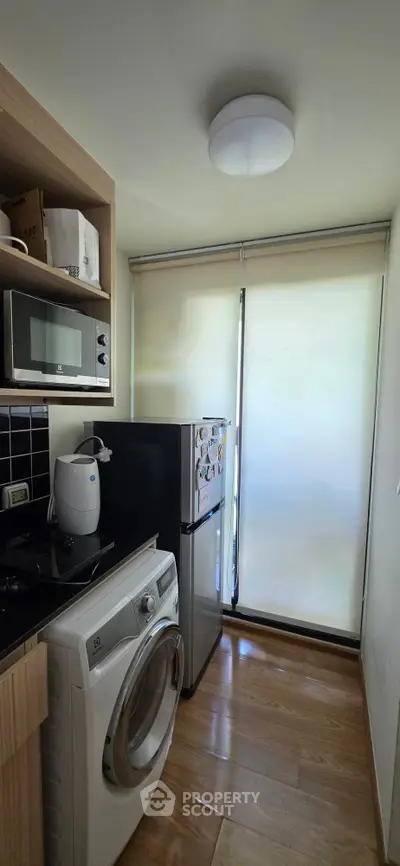 Compact kitchen with modern appliances including washing machine and microwave, featuring sleek wooden flooring.
