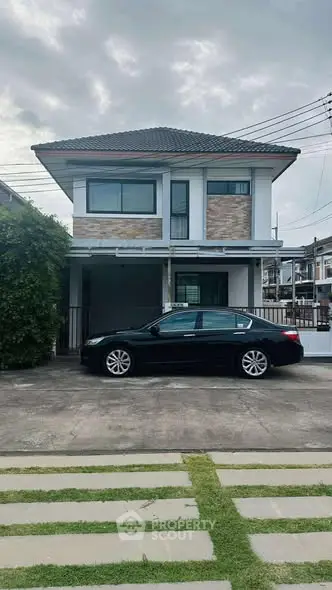 Modern two-story house with car parked in driveway, featuring a stylish facade and lush greenery.
