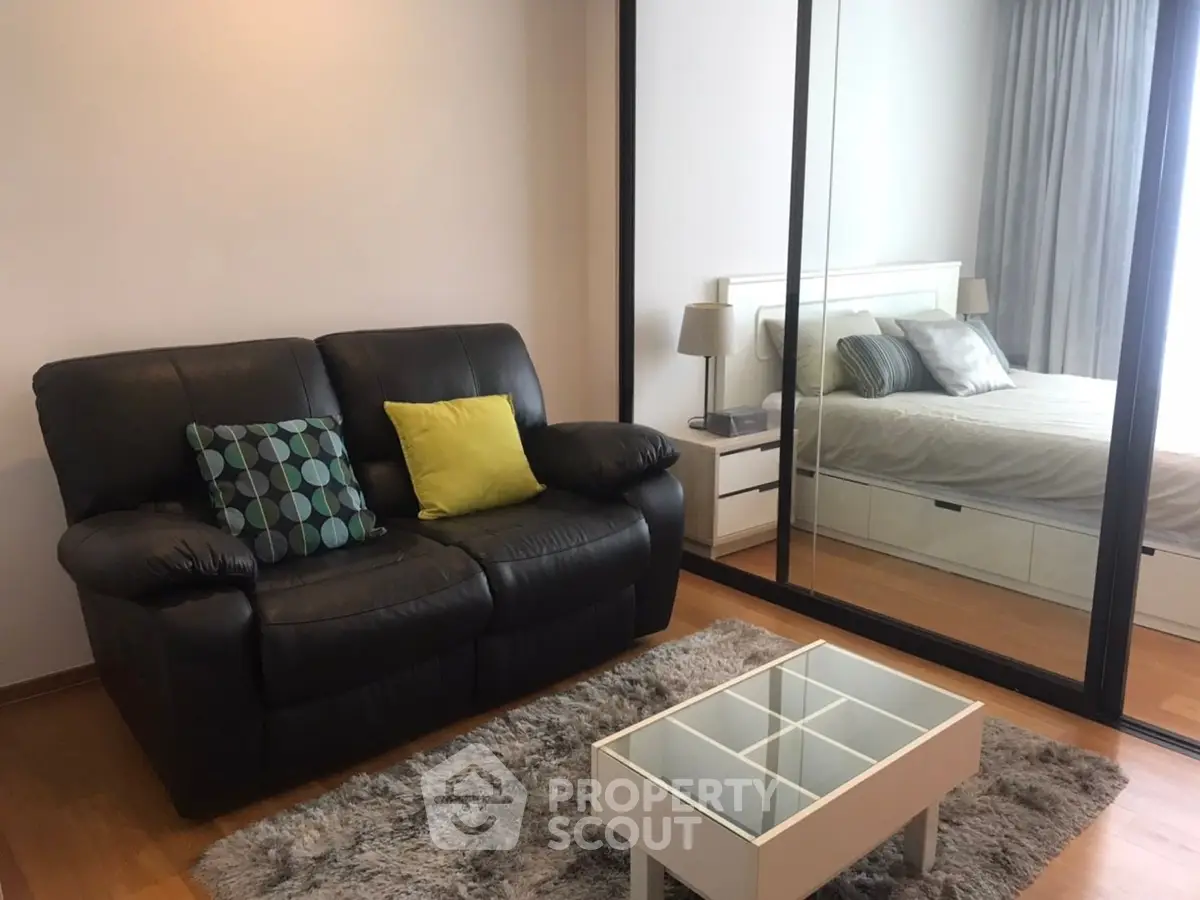 Modern living room with cozy sofa and mirrored wardrobe reflecting a stylish bedroom.