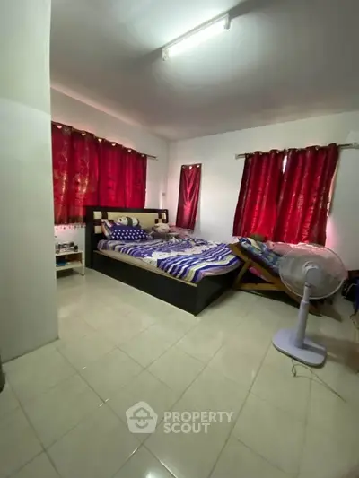Spacious bedroom with tiled flooring and vibrant red curtains