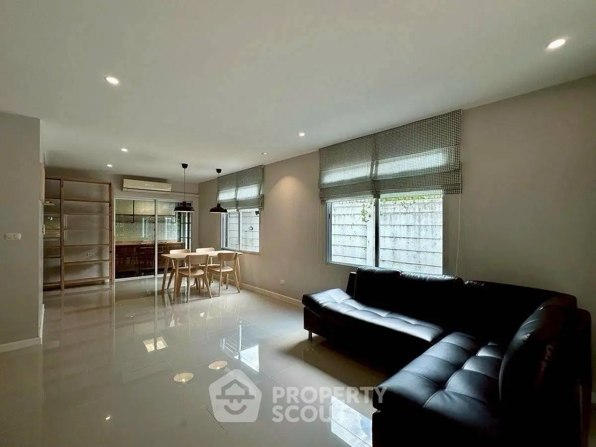 Spacious modern living room with sleek black sofa and dining area, perfect for entertaining.