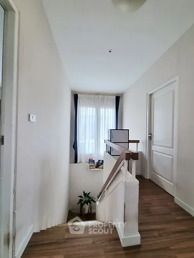 Bright hallway with wooden flooring and staircase, featuring natural light from window.