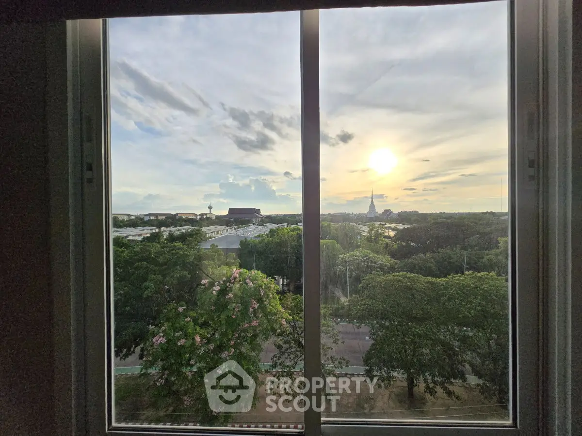 Stunning view from a window overlooking lush greenery and a distant cityscape at sunset.
