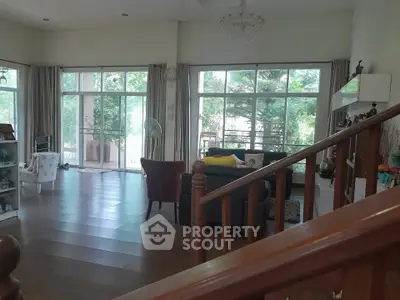Spacious living room with large windows and elegant decor, offering a serene view of lush greenery.