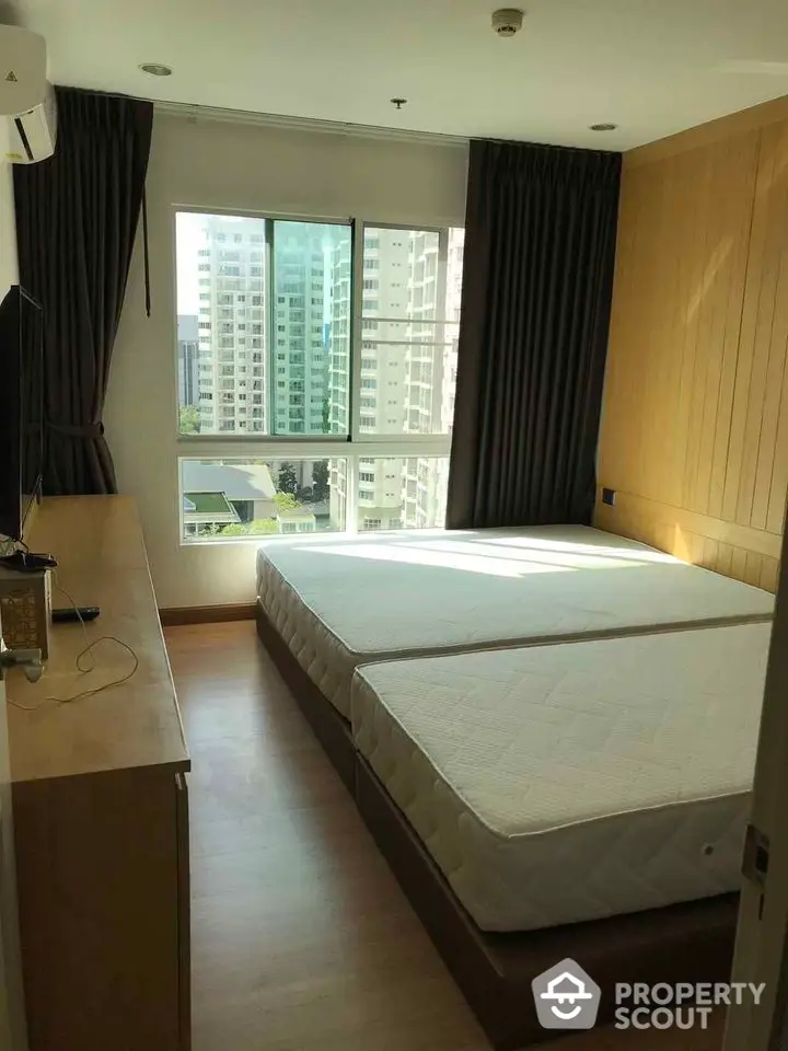 Spacious bedroom with large windows and city view, featuring twin beds and modern decor.