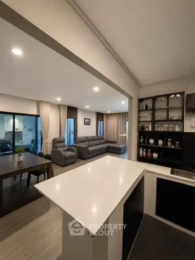 Spacious open-plan living room with modern kitchen and dining area, featuring sleek furnishings and ample natural light.