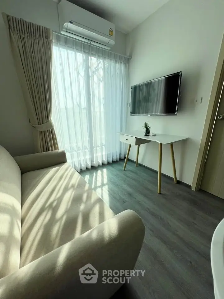 Modern living room with natural light, featuring a cozy sofa, wall-mounted TV, and stylish decor.