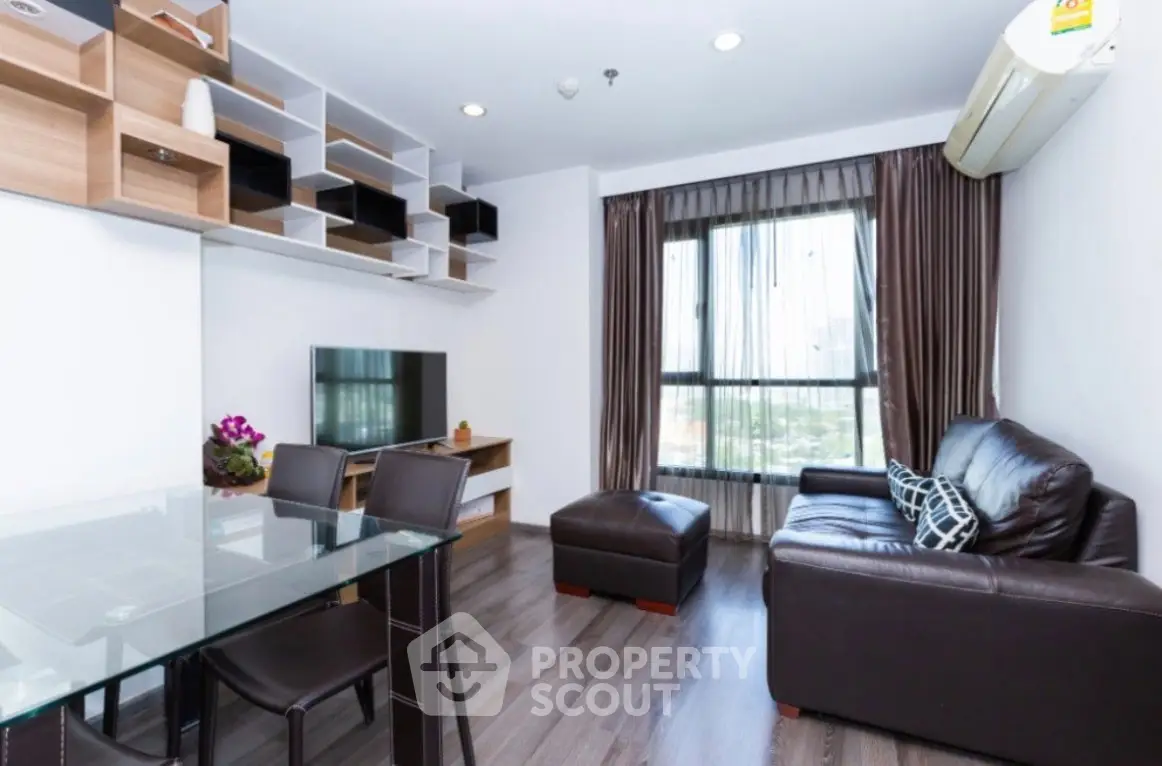 Modern living room with sleek furniture and large window offering city views.
