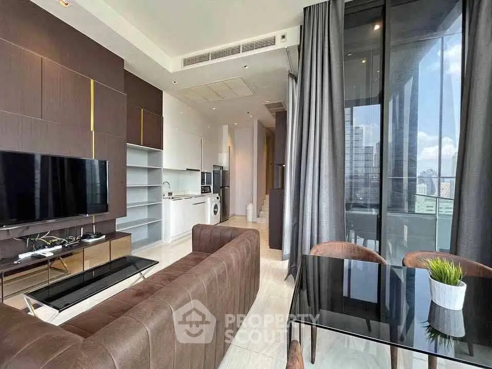Modern living room with open kitchen and city view, featuring sleek furniture and floor-to-ceiling windows.