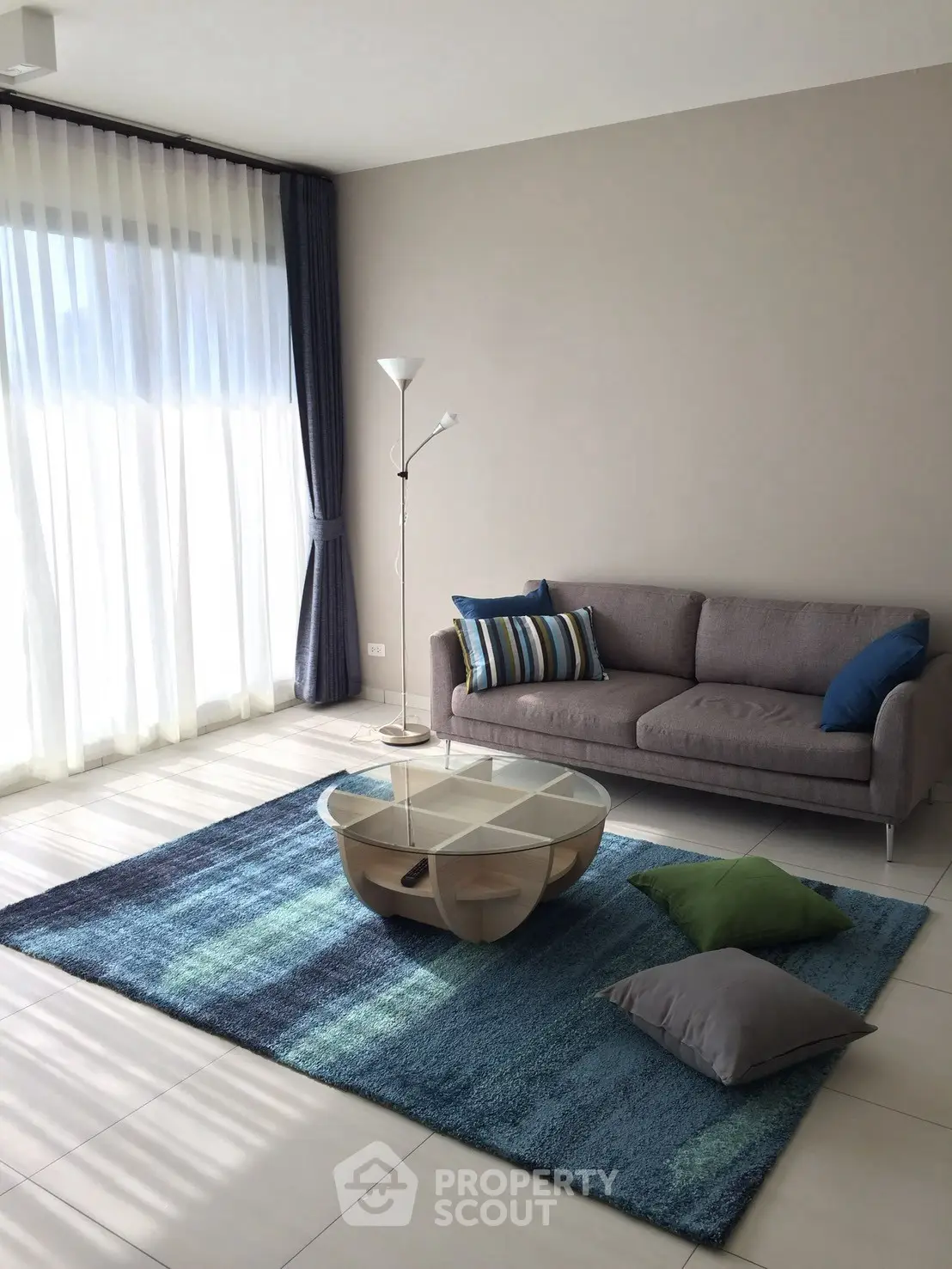 Modern living room with stylish sofa, glass coffee table, and large windows with sheer curtains.
