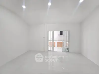 Spacious minimalist living room with sleek white tiles and sliding glass doors leading to kitchen.